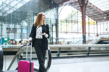 Young woman with suitcase and cell phone at train station - KIJF02862