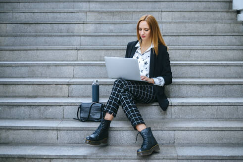 Junge Geschäftsfrau sitzt auf einer Treppe und benutzt einen Laptop - KIJF02871
