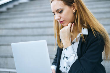 Junge Geschäftsfrau sitzt auf einer Treppe und benutzt einen Laptop - KIJF02876