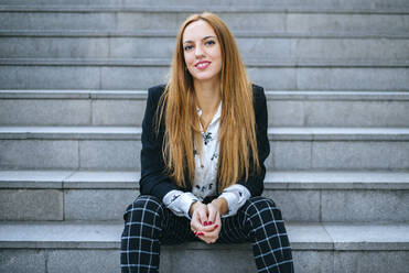 Porträt einer lächelnden jungen Frau auf einer Treppe sitzend - KIJF02878