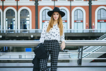 Portrait of smiling young woman wearing a hat at train station - KIJF02882