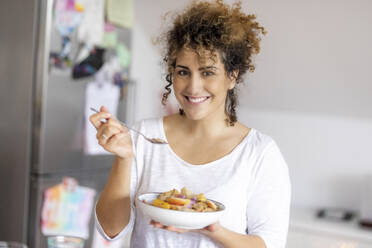 Portrait of smiling woman with bowl of fruit muesli in the kitchen - FMKF06052