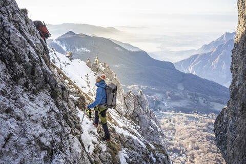 Alpinist, der in einem felsigen, verschneiten Berg steht und nach oben schaut, Orobie Alpen, Lecco, Italien, lizenzfreies Stockfoto