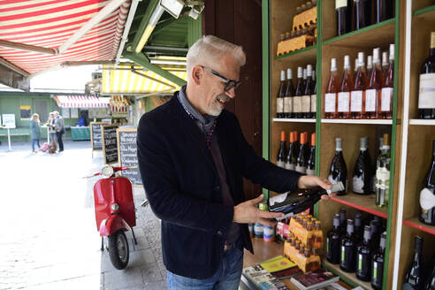 Reifer Mann wählt eine Flasche Wein in einer Weinhandlung aus - ECPF00828