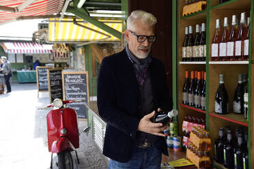 Reifer Mann wählt eine Flasche Wein in einer Weinhandlung aus - ECPF00829