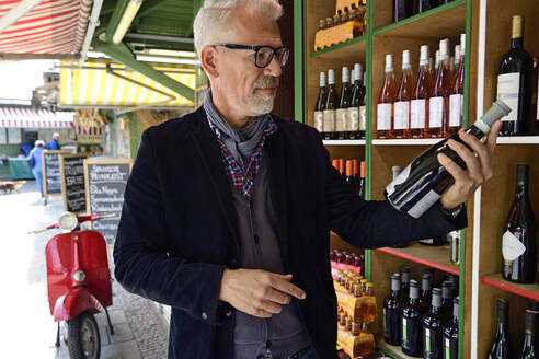 Reifer Mann wählt eine Flasche Wein in einer Weinhandlung aus - ECPF00830
