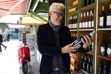 Lächelnder reifer Mann, der eine Flasche Wein in einer Weinhandlung auswählt - ECPF00832