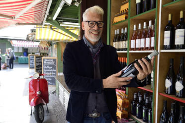 Porträt eines lächelnden reifen Mannes, der eine Flasche Wein in einer Weinhandlung auswählt - ECPF00833