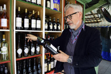 Mature man choosing bottle of wine at a wine shop - ECPF00837