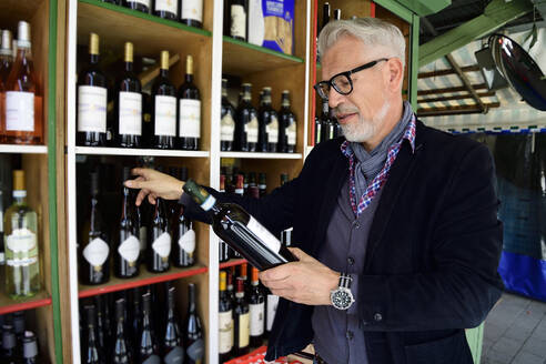 Reifer Mann wählt eine Flasche Wein in einer Weinhandlung aus - ECPF00837