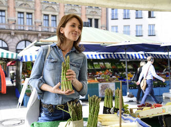 Mature woman choosing asparagus at a market stall - ECPF00855