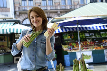 Portrait of smiling mature woman choosing asparagus at a market stall - ECPF00857