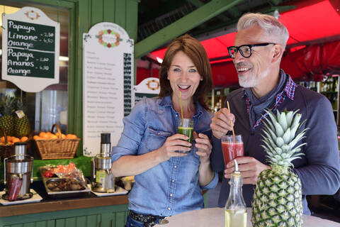 Porträt eines glücklichen reifen Paares, das an einem Marktstand einen gesunden Saft trinkt, lizenzfreies Stockfoto