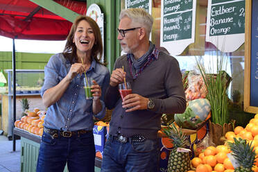 Porträt eines glücklichen reifen Paares, das an einem Marktstand einen gesunden Saft trinkt - ECPF00864