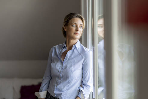 Mature woman looking out of the window at home - FMKF06065