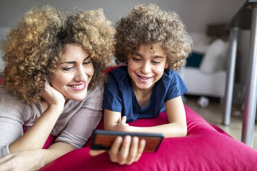Mutter und Sohn sehen sich ein Video auf dem Smartphone an und liegen auf einem großen Kissen - FMKF06069
