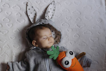Porträt eines schlafenden kleinen Mädchens in einem Kaninchen-Kapuzenpulli auf einer weißen Decke liegend - GEMF03381