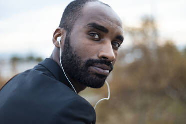 Portrait of bearded young businessman with earphones outdoors - JSRF00717