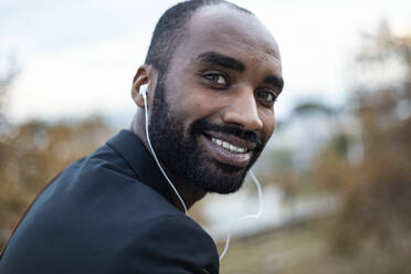 Portrait of smiling young businessman with earphones outdoors - JSRF00718