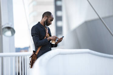 Junger Geschäftsmann mit Kopfhörern und Kaffee zum Mitnehmen, der sein Smartphone im Freien benutzt - JSRF00719