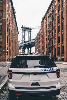 USA, New York, New York City, Polizeiauto auf der Straße mit Manhattan Bridge im Hintergrund - CJMF00228