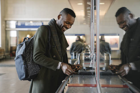 Happy stylish man buying ticket in train station - AHSF01606