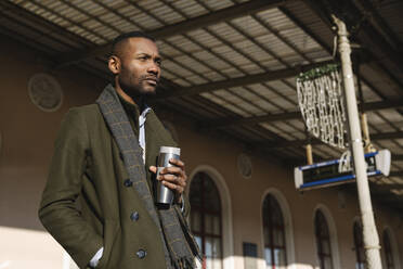 Stylish man with reusable cup waiting for the train - AHSF01616