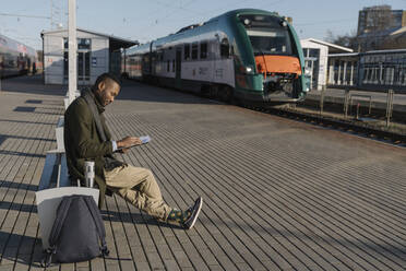 Stylish man reading documents while waiting for the train - AHSF01623
