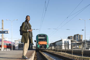 Porträt eines stilvollen Mannes mit wiederverwendbarem Becher, der auf den Zug wartet - AHSF01629