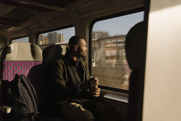 Stylish man with reusable cup inside a train - AHSF01635