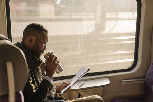 Stylish businessman with reusable cup and documents in a train - AHSF01639