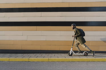 Stylish man with helmet and scooter passing a building - AHSF01660