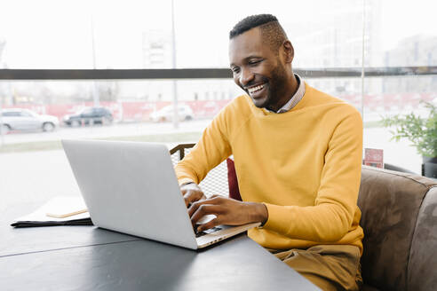 Happy man using laptop in a cafe - AHSF01664