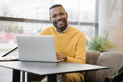 Porträt eines glücklichen Mannes mit Laptop in einem Café, lizenzfreies Stockfoto