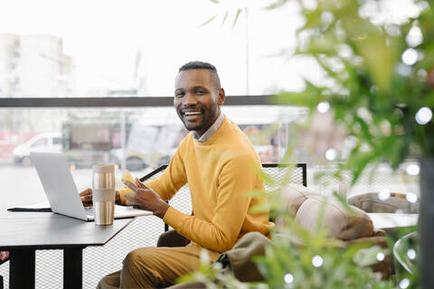 Porträt eines glücklichen Mannes mit Smartphone und Laptop in einem Cafe, lizenzfreies Stockfoto