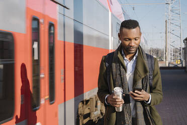 Porträt eines stilvollen Mannes mit Smartphone neben einem Zug - AHSF01686