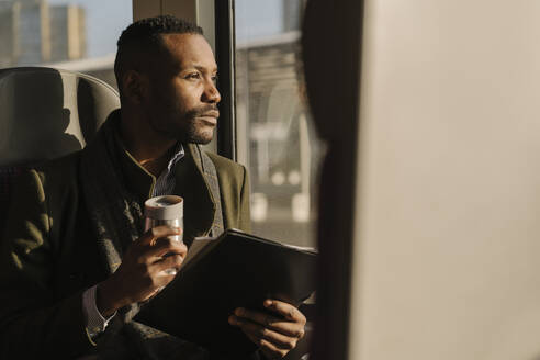 Portrait of stylish businessman with reusable cup and documents inside a train - AHSF01688