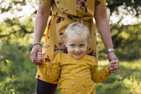 Porträt eines kleinen blonden Mädchens Hand in Hand mit ihrer Mutter auf einer Wiese - NMSF00400
