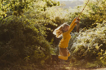 Happy little girl swinging on a rope swing in nature - NMSF00402