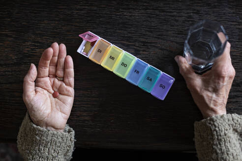 Senior woman taking medicine, water glass and pill organiser - MAMF00994