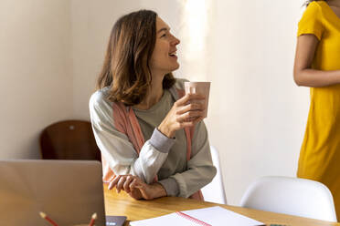 Glückliche Geschäftsfrau mit Kaffeebecher im Büro - AFVF04710