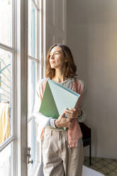 Woman holding folder looking out of window - AFVF04736