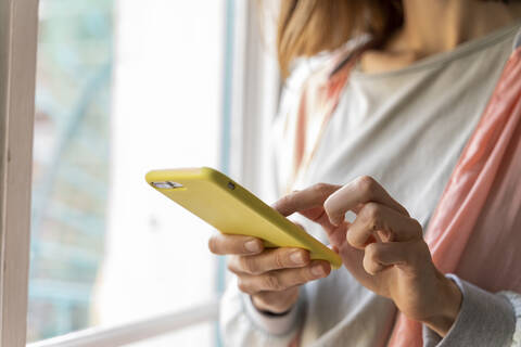 Nahaufnahme einer Frau, die am Fenster ein Mobiltelefon benutzt, lizenzfreies Stockfoto