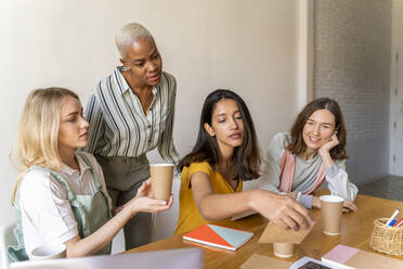 Businesswomen having a meeting in office working on reusable cups - AFVF04743