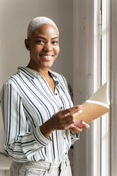 Porträt einer lächelnden Frau mit Notizbuch am Fenster - AFVF04756