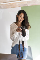 Portrait of smiling young architect with camera and laptop in a studio - AFVF04769