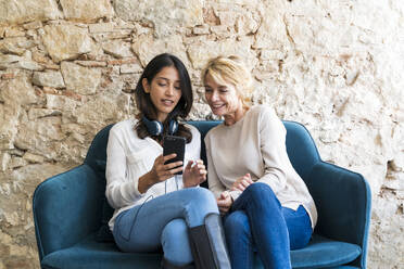 Portrait of two colleagues sitting on couch at looking at smartphone - AFVF04783