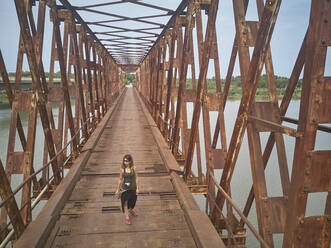 Benin, Grand Popo, Female tourist crossing rusty iron bridge - VEGF01233