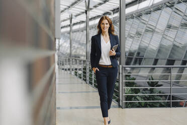 Confident businesswoman holding a tablet in a modern office building - JOSF04142