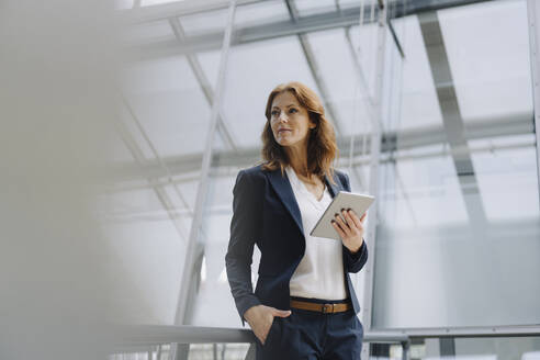 Confident businesswoman holding a tablet in a modern office building - JOSF04145